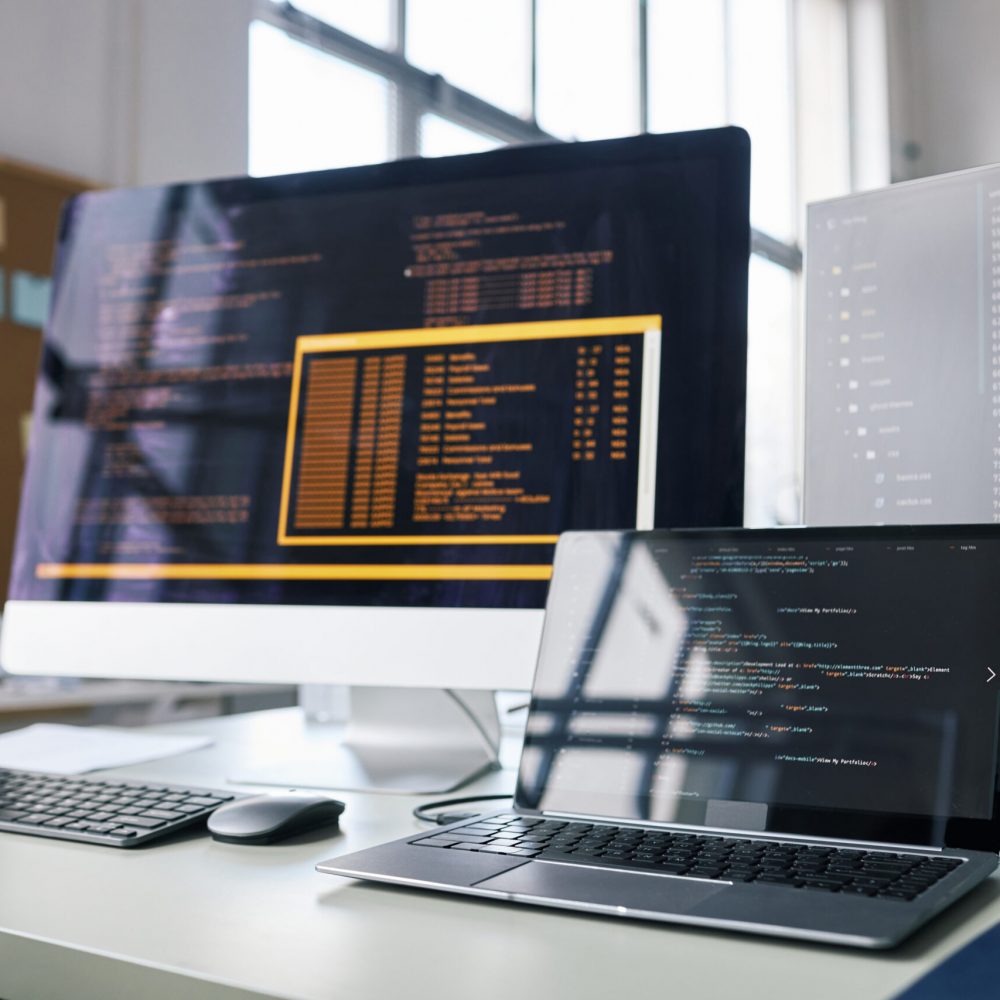 Laptop and computer monitors on desk of software develoepr in office of IT company